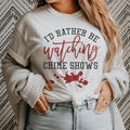 Woman wearing a cozy "I'd Rather Be Watching Crime Shows" tee, perfect for true crime fans and Netflix marathons